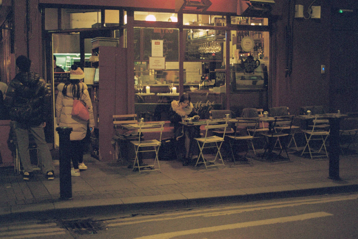 Colour photograph of young woman reading outside French-style cafe at night